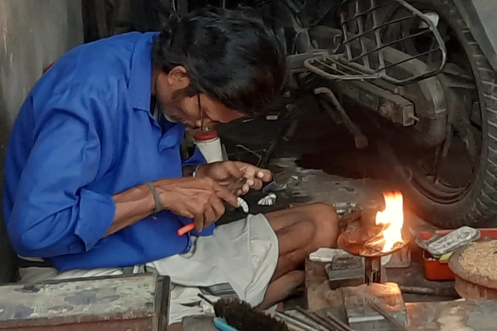 An Indian goldsmith in Kollam working on a piece of gold jewellery at a bench beside a small flame