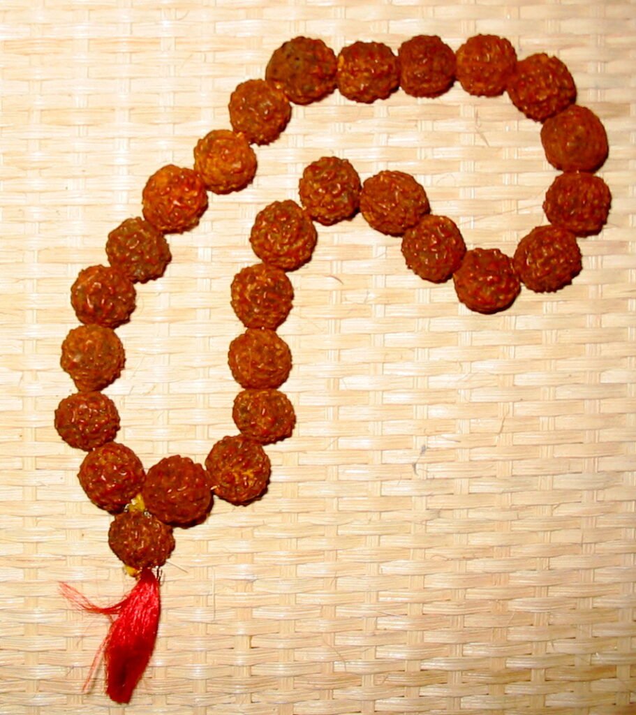 A short strand of brown rudraksha beads with a red tassel, laid on a woven mat