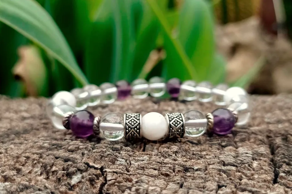 A bracelet of clear quartz, amethyst and white beads resting on a tree stump