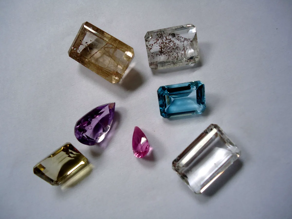 Seven loose faceted gemstones in different colours and cuts on a grey background