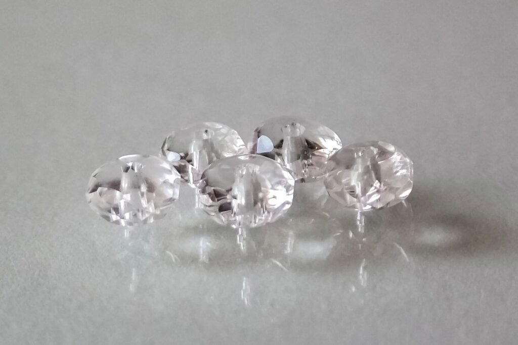 Five faceted, drilled rock crystal (clear quartz) beads on a pale grey surface
