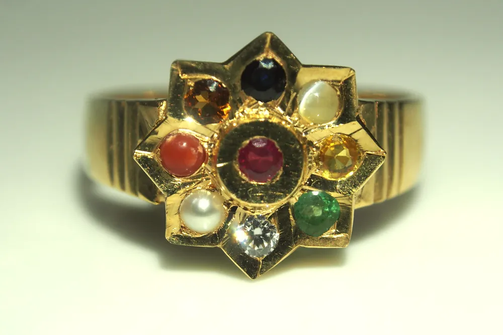 A gold navaratna ring set with nine different coloured gemstones