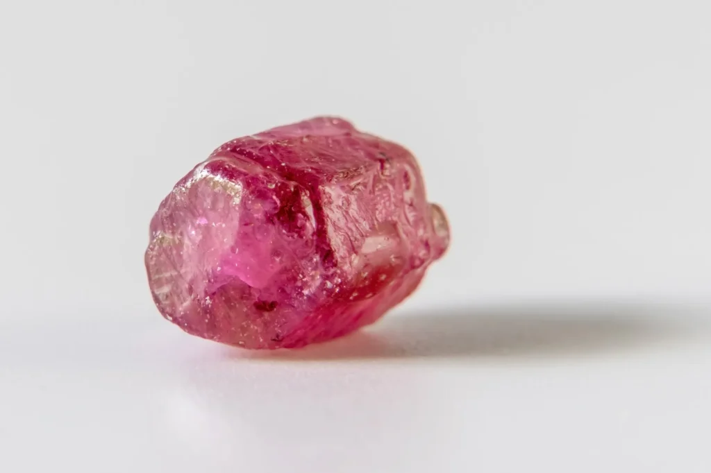 A rough pinkish-red ruby crystal on a white surface
