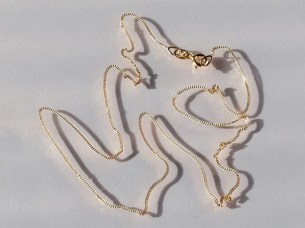 A polished curb chain in 18K gold on a white background