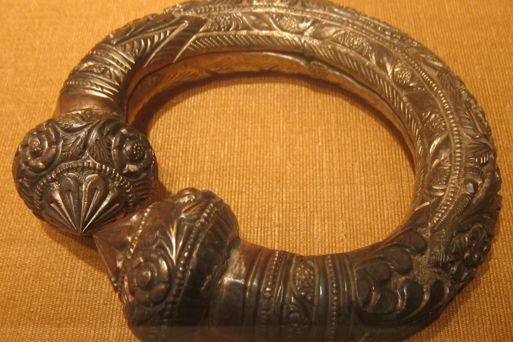 A 19th-century Indian silver anklet with a gold wash, the gold worn away to dark silver on the raised decoration