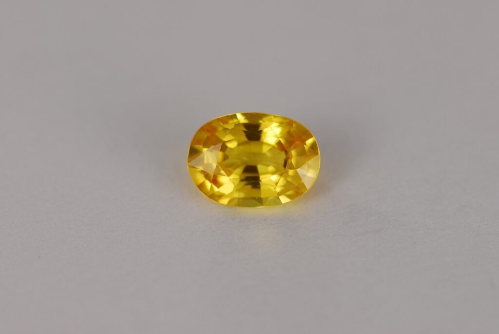 An oval faceted yellow sapphire of about one carat on a grey background