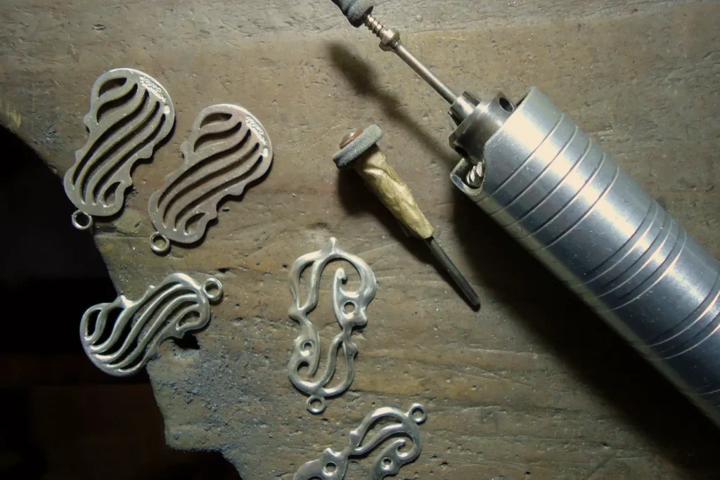 Silver pendants on a jeweller's bench beside a pendant motor polishing tool, the preparation step before plating