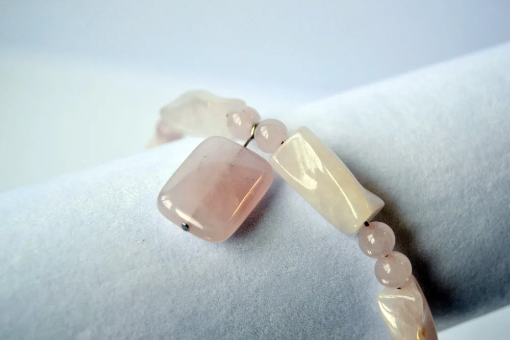 A bracelet of pale pink rose quartz beads, square, oblong and round, resting on a white velvet display roll