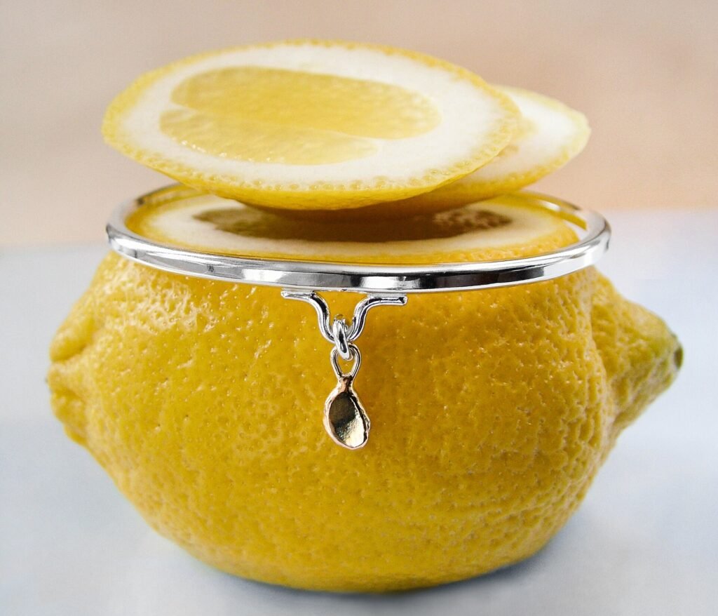 A polished sterling silver bangle with a small gold drop, resting on a lemon